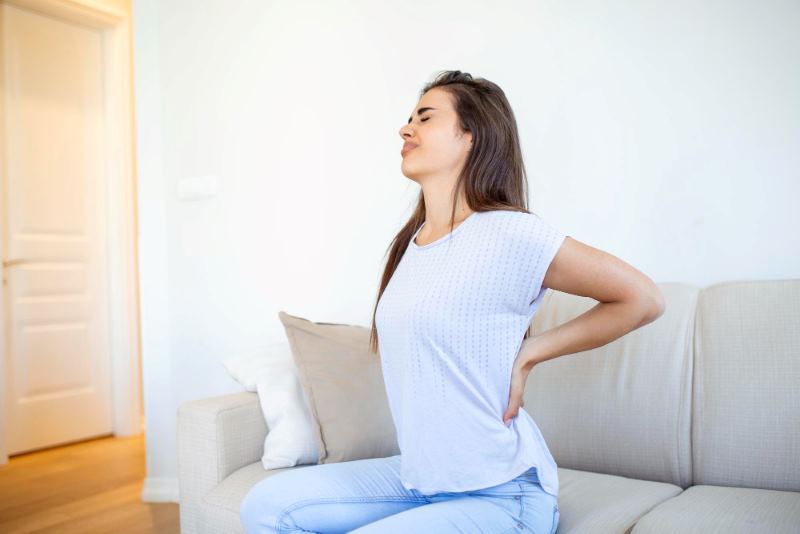 Woman Seated on Couch Suffering From Back Pain